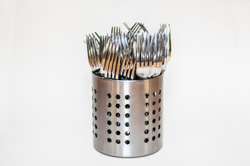 Silvery forks stand in a metal stand on a white background. And one fork is higher than the rest....