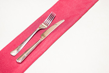Metal fork and knife on a silk napkin on the table.