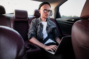 Fototapeta na wymiar Young business person using laptop on a backseat of a car. Milennial person using modern technology while commuting by a private or rental car