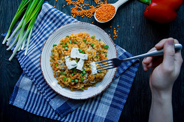 A man eats a lentil porridge with vegetables and greens and fett cheese. Healthy lifestyle. Dietary menu. Dark wooden background. View from above.