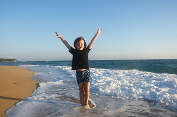 Boy in black t-shirt have fun by the sea. Child play on coastline while big wave splashing on beach