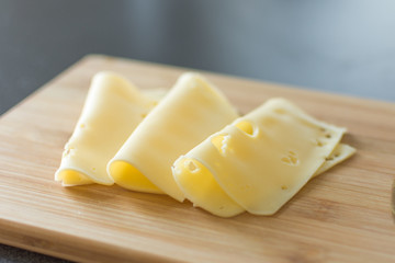 Slices of cheese on wooden background. Holland cheese with holes.