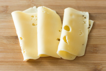 Slices of cheese on wooden background. Holland cheese with holes.