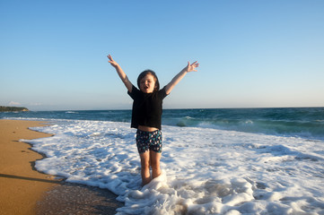 Fototapeta na wymiar Boy in black t-shirt have fun by the sea. Child play on coastline while big wave splashing on beach
