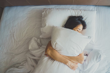 Woman stretching in bed after waking up, back view. Woman sitting near the big white window while...