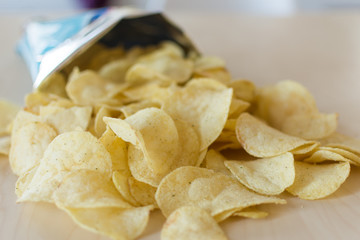 Heap of potato crisps on wooden background. Potato chips, unhealthy eatting.