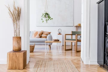 Foto op Canvas The modenr boho interior of living room in cozy apartment with design coffee table, gray sofa, wooden cube honey yellow pillow, desk, green armchair, plants and elegant accessories. Modern home decor. © FollowTheFlow