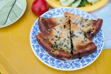 Vegetable appetizer on a dish. Fresh green onions, tomatoes, cucumbers, lettuce. Baked Cake On the background of the table is yellow. Evening, summer.
