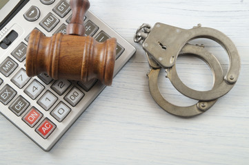 Wooden gavel, calculator and handcuffs on white table. financial fraud concep