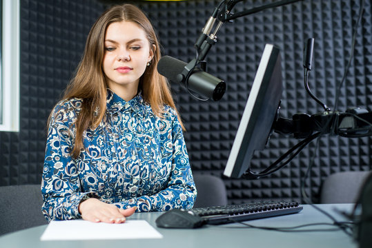Young pretty woman radio presenter sitting in studio with headphones and talking on the air