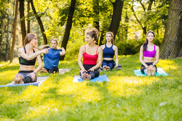 Cheerful group of mature female friends relaxing after yoga sits on mats in summer park in the morning. Teamwork, good mood and healthy life concept.