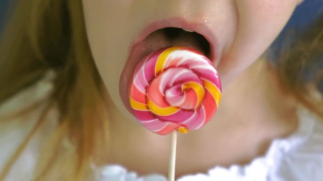Little girl with a lollipop on a blue background. Close up portrait