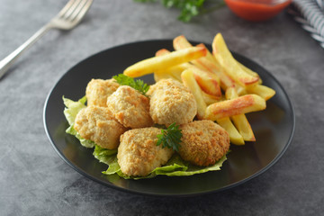 Chicken nuggets with french fries on dark background, top view.