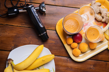 fresh fruit smoothie with banana and apricots at orange  tray  with blender  at wooden table. flat lay