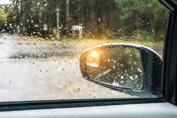 wet side mirror of car in raindrops, outside autumn time in city rainy park, sun is shining