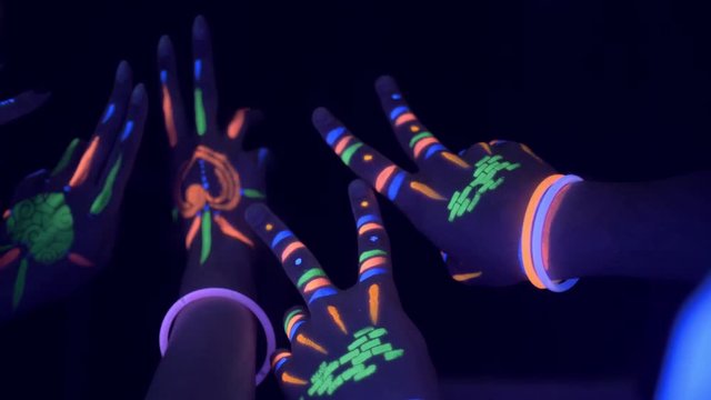 Hand with colorful neon bracelets in the air during a neon party with blurry lights in the background