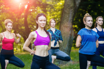 Yoga or pilates at park, group of mixed age women doing different pose while standing in morning time. Teamwork, sport, good mood and healthy life concept. Seria photo with real people models.