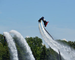 Synchronized flip on flyboards against a blue sky and green trees. Summer extreme sports