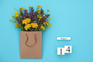 Wooden cubes calendar August 14 and field colorful rustic flowers in craft package on blue background. Greeting card Flat Lay Concept Hello August Template with copy space for text and design