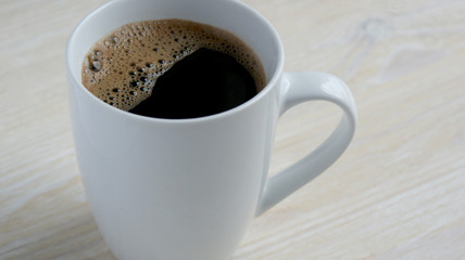 delicious fragrant black coffee with foam in a white mug on a wooden table in the morning on a Sunny day