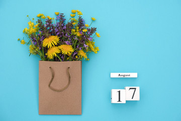 Wooden cubes calendar August 17 and field colorful rustic flowers in craft package on blue background. Greeting card Flat Lay Concept Hello August Template with copy space for text and design