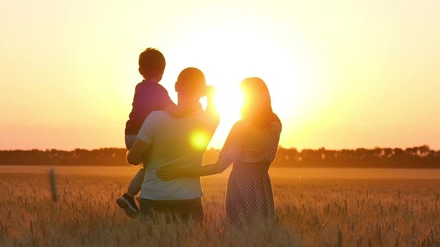 A man, a woman and a child stand on a wheat field and point their fingers at the sunset. The father holds his son in his arms. Happy family.
