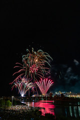 Imagen vertical de mucha gente observando los fuegos artificiales sobre el puente en el río con la ciudad vieja al lado