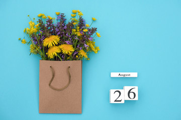 Wooden cubes calendar August 26 and field colorful rustic flowers in craft package on blue background. Greeting card Flat Lay Concept Hello August Template with copy space for text and design