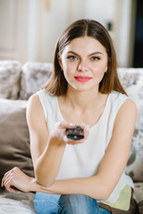 Young girl sitting on sofa and using tv remote at home