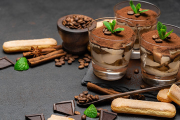 Classic tiramisu dessert in a glass and savoiardi cookies on dark concrete background