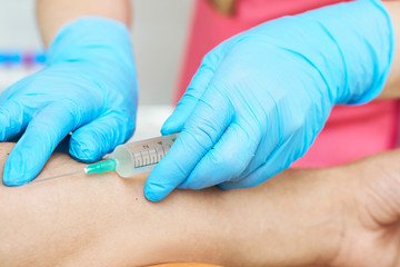 nurse with a syringe in her hand is going to take a patient's blood sample for a blood test at the hospital.