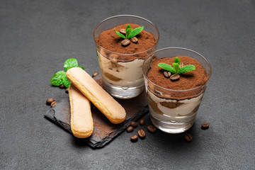 Classic tiramisu dessert in a glass and savoiardi cookies on dark concrete background