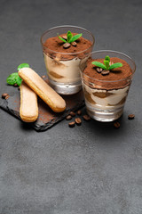Fototapeta na wymiar Classic tiramisu dessert in a glass and savoiardi cookies on dark concrete background
