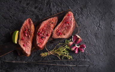 Beef steaks with pomegranate seeds, vegetables and thyme on a black slate table. The view from the top. - 275912828