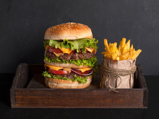 A large Hamburger and French fries on a wooden tray on a dark wooden table. Fast food. Copy space