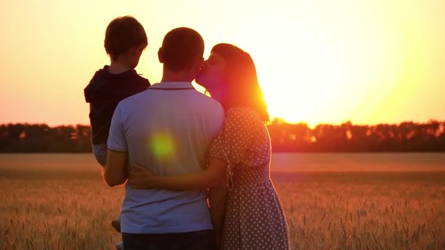 Happy family watching the sunset, standing on a wheat field. A man holding a child. A woman hugs a man and kisses him.