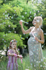 Little girl and her pregnant mother playing blowing soap bubbles