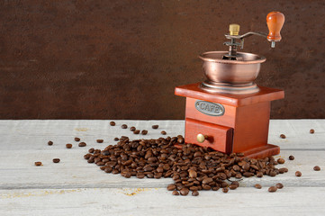 Manual coffee grinder and coffee beans scattered on a wooden table