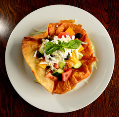 Mixed salad of tomatoes, peppers, olives, basil and cheese in fried tortilla on white plate