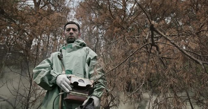 Serious man with Geiger counter standing in forest