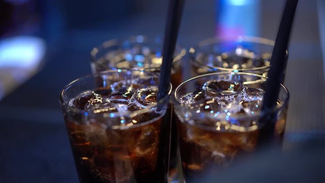 a glass with a cocktail cube libre with ice inserts a straw. Cold brown cocktail. Close-up.