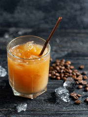 Summer drink iced coffee in a glass on a dark old wooden table with coffee beans