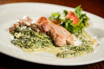 Pork steak with spinach cream sauce and vegetables on white plate