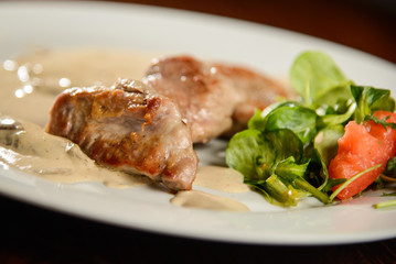Pork medallions with mushroom cream sauce and green salad on white plate