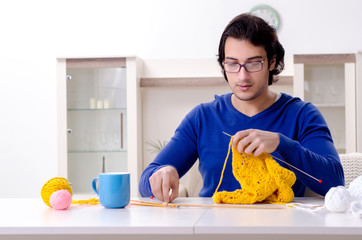 Young good looking man knitting at home