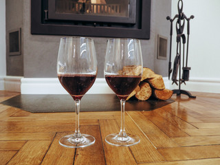 Glasses of wine near the fireplace with firewood.Holiday and cozy concept.