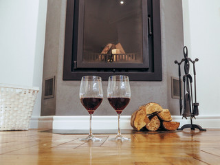 Glasses of wine near the fireplace with firewood.Holiday and cozy concept.