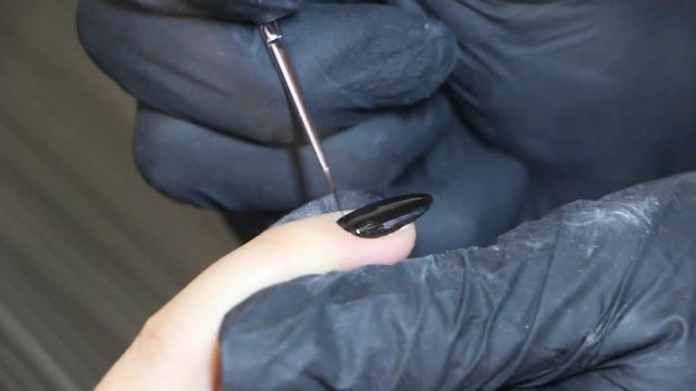 Manicurist's hands are covering gel-polish on the client's nails.