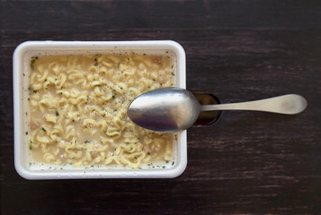 Chinese instant noodles, brewed in a plastic rectangular Cup. Noodles and spoon closeup on wooden brown background. Place for text.