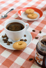 Cookies with jam and cup of hot coffee on wooden table covert red tablecloth